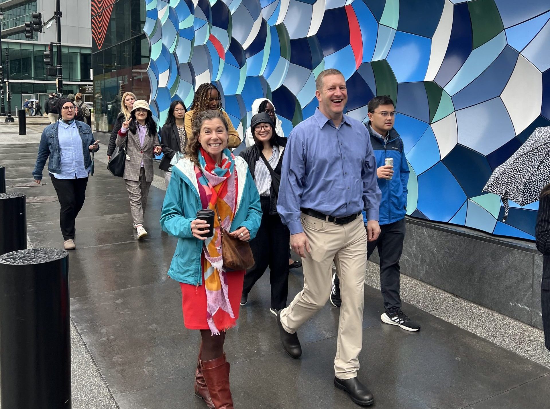 A group of people smiling and walking outside against a colorful wall.